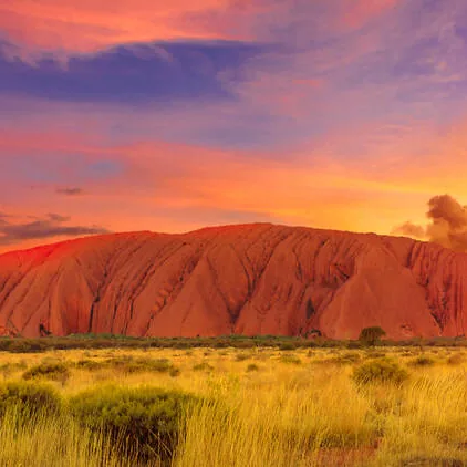 Uluru under a red and orange sunset sky